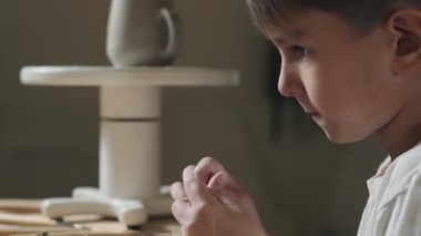 Çömlekçilik dersinde küçük çocuğun kille oynadığı yan manzara