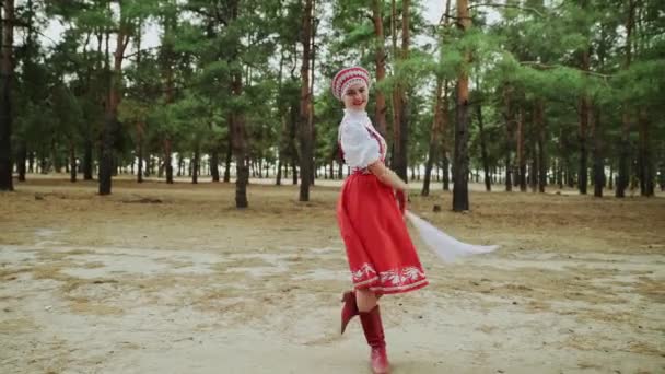 Красивая женщина в красном русском традиционном народном костюме с платком танцует в лесу — стоковое видео