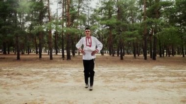 Geleneksel Rus kostümü giymiş genç adam yaz ormanlarında Rus dansları yapıyor.