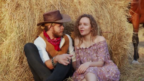 Um jovem casal se senta em feno na fazenda. feliz sorrindo cowboy e mulher passar tempo juntos — Vídeo de Stock