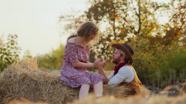 Una joven pareja se sienta en el heno de la granja. Feliz vaquero sonriente y mujer pasar tiempo juntos — Vídeo de stock