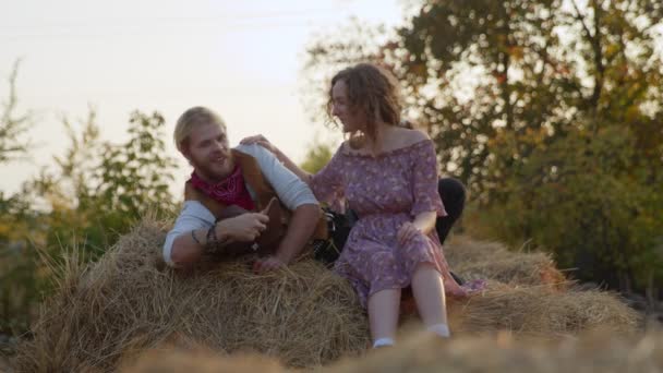 Een jong stel ligt te knuffelen met hooi. Gelukkig lachende cowboy en vrouw brengen tijd samen door — Stockvideo