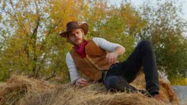 Çiftliğinde samanların yanında poz veren yakışıklı kovboy.
