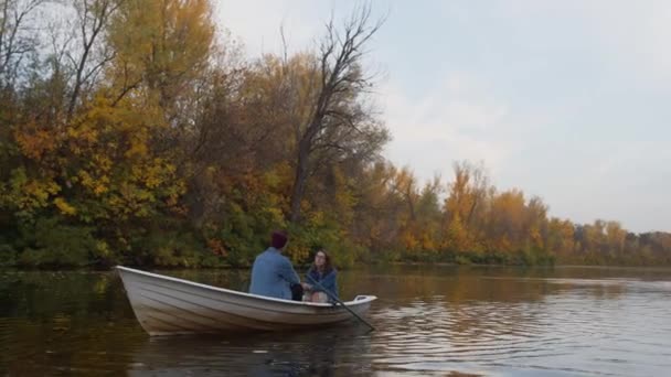 Um cara bonito e uma linda garota se senta em um barco em um lago em uma floresta de outono fada — Vídeo de Stock