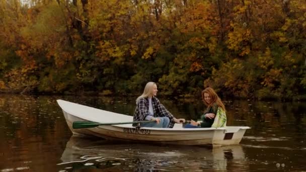 Duas belas mulheres loiras e gengibre se senta em um barco em um lago em uma floresta de outono fada — Vídeo de Stock