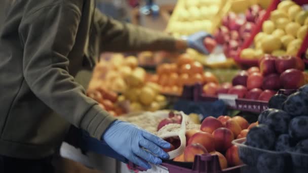 Jonge vrouw met blauwe handschoenen zet rode verse granaten in string tas op de markt — Stockvideo