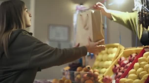 Молодая женщина дает бумажный пакет продавцу на рынке — стоковое видео