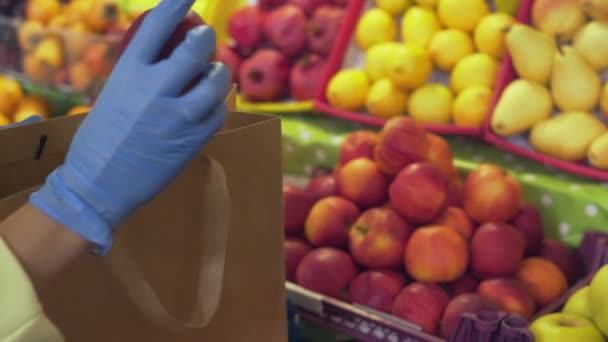 Gros plan de la femme en gants bleus met des pommes rouges dans un sac à ficelle au marché — Video