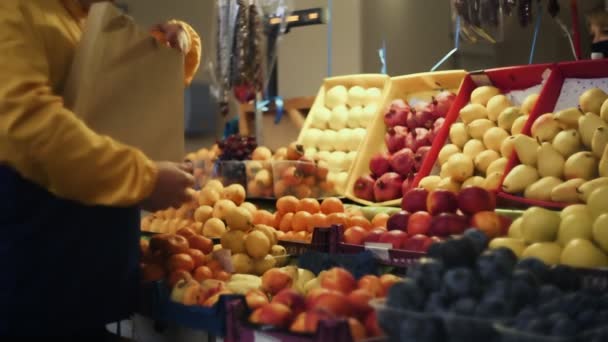 Een man kiest een verse mandarijnen, stopt ze in een papieren zak en geeft het aan de verkoper op de markt. — Stockvideo