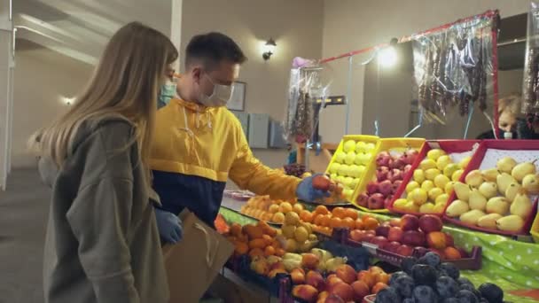 Молодая пара защитных масок и перчаток выбирает фрукты на рынке — стоковое видео