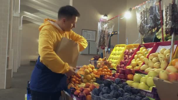 Een man kiest een verse mandarijnen, stopt ze in een papieren zak en geeft het aan de verkoper op de markt. — Stockvideo
