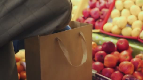 Gros plan de la femme en gants bleus met des pommes rouges dans un sac en papier au marché — Video