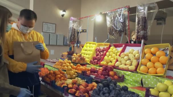 Jonge paar met beschermende masker en handschoenen kiest een verse mandarijnen, zet ze in een papieren zak ang geeft het aan verkoper in de markt — Stockvideo