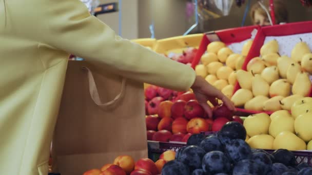 黄色のコートの女性のバックビューは、市場で紙袋に赤いリンゴを置きます — ストック動画