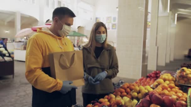 Νεαρό ζευγάρι με προστατευτική μάσκα και μπλε γάντια που μαλώνουν στην αγορά — Αρχείο Βίντεο