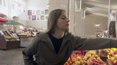 Genç bir kadın marketteki raflardan portakal koklar ve seçer.