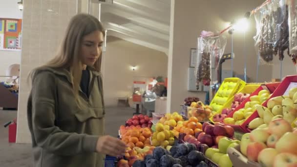 Молодая женщина нюхает и выбирает сливы на полках магазинов на рынке — стоковое видео