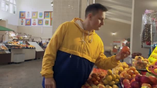 Молодой человек нюхает и выбирает свежие яблоки на рынке — стоковое видео