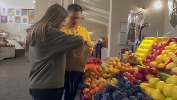 Νεαρό ζευγάρι επιλέγει πολλά διαφορετικά φρούτα και τους σε μια χάρτινη σακούλα στην αγορά — Αρχείο Βίντεο