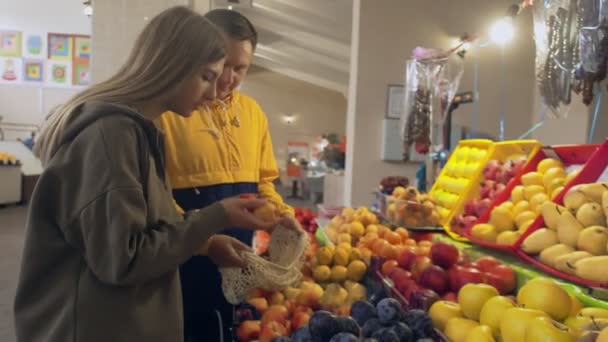 若いカップルはいくつかの桃を選択し、市場でストリングバッグに入れます — ストック動画