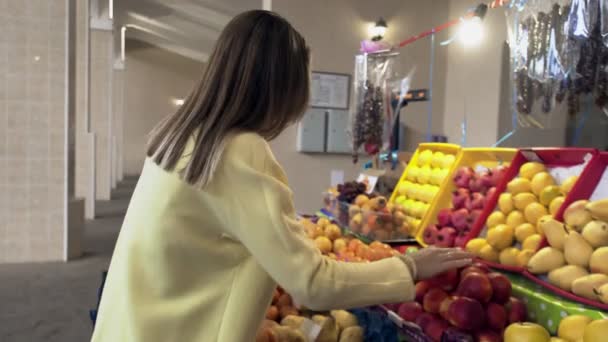 Femme en manteau jaune choisit un fruit frais au marché — Video