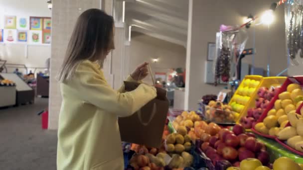 Vrouw in gele jas doet een verse rode appels in een papieren zak, dan geeft het aan verkoper op de markt — Stockvideo