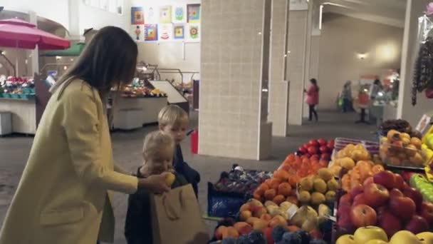 Мальчик и девочка с матерью выбирают свежие фрукты на рынке. — стоковое видео