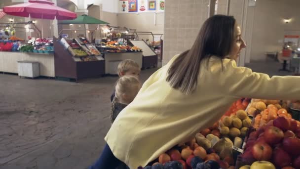 Mały chłopiec i dziewczynka z matką wybiera świeże owoce na targu. — Wideo stockowe