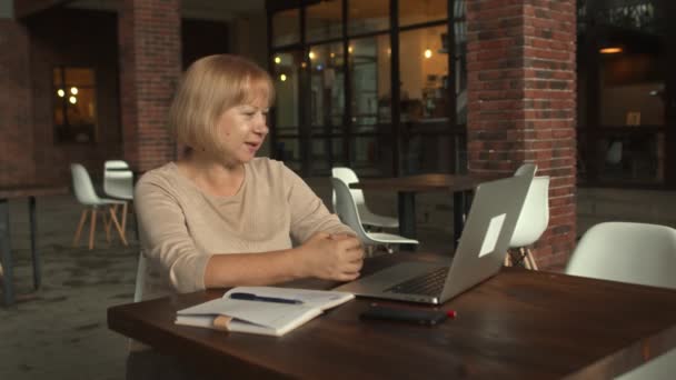 Mulher de negócios sênior positiva trabalhando com um laptop enquanto tem uma chamada de vídeo no café — Vídeo de Stock