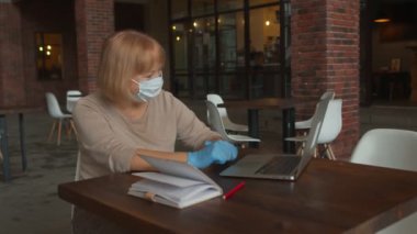 Koruyucu maskeli ve eldivenli kıdemli bayan öğretmenin bir mesafe dersi var. Kafede bir video görüşmesi var.