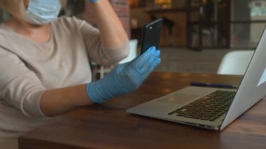 Koruyucu maskeli ve eldivenli bir bayan kafede telefon kullanıyor.