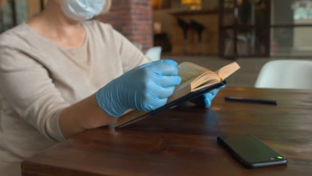 Close up de mulher com máscara protetora e luvas lê livro no café — Vídeo de Stock