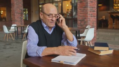 Kıdemli adam telefonla konuşuyor ve kafede not defteri tutuyor.