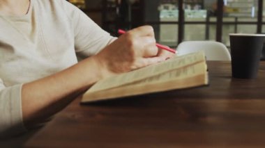 Son sınıf öğrencisi kadın kitap okuyor ve sokak kafesinde işaretler bırakıyor.