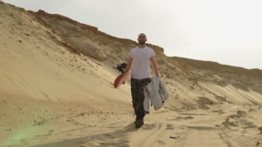 Yakışıklı kaslı adam çölde ya da taş ocağında kumla yürüyor.