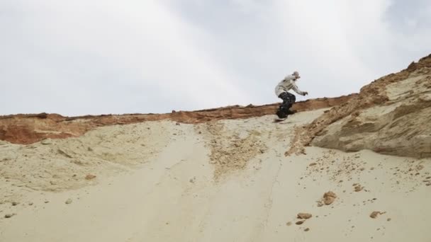 Bello uomo sandboards una montagna nel deserto o cava di sabbia — Video Stock