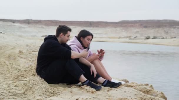 Молодая пара сидит на песке в пустыне и разговаривает — стоковое видео