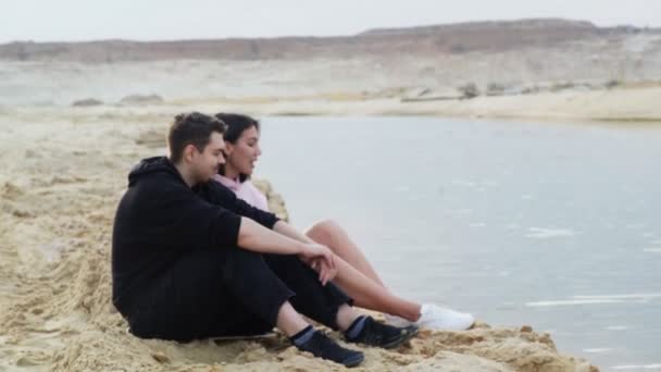 Mladý pár sedí na písku v poušti a mluví — Stock video
