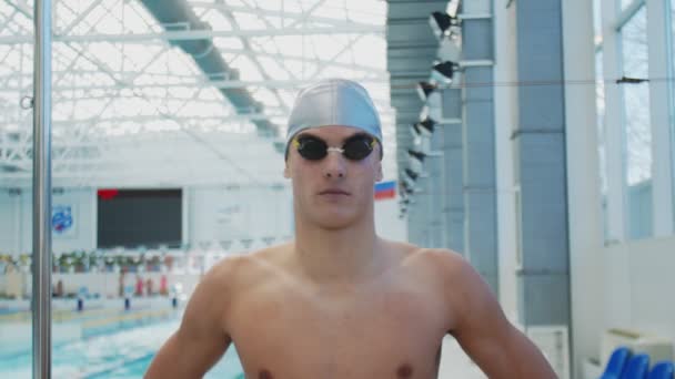 Guapo atleta nadador con gafas y sombrero mira a la cámara — Vídeos de Stock