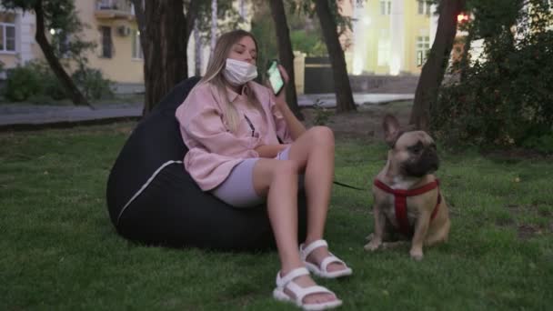 Mujer joven se sienta en la silla de la bolsa de frijol con su bulldog francés y habla por teléfono — Vídeo de stock