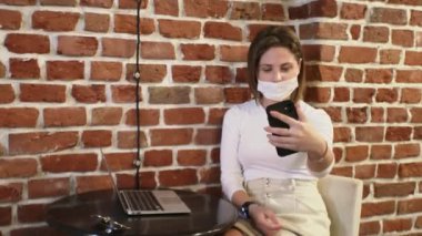 Koruyucu maskeli ve beyaz balıkçı yakalı genç bir kadın kafede selfie çekiyor.