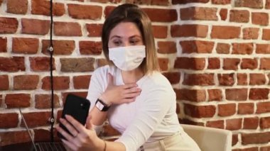 Koruyucu maskeli ve beyaz balıkçı yakalı genç bir kadın kafede selfie çekiyor.