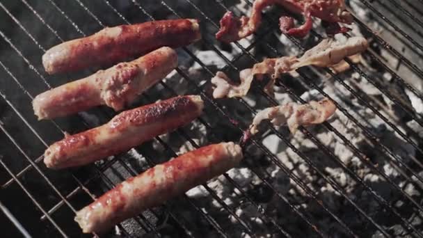 Gotowanie grillowanie bekon i kiełbasy na grillu siatki na zewnątrz dla przyjaciół piknik party — Wideo stockowe