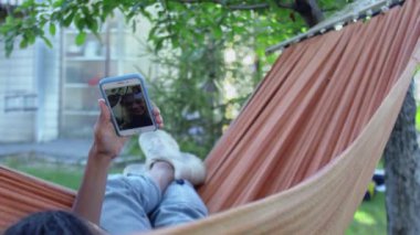 Hamakta yatarken telefonla arkadaşlarıyla konuşan genç bir kadın.