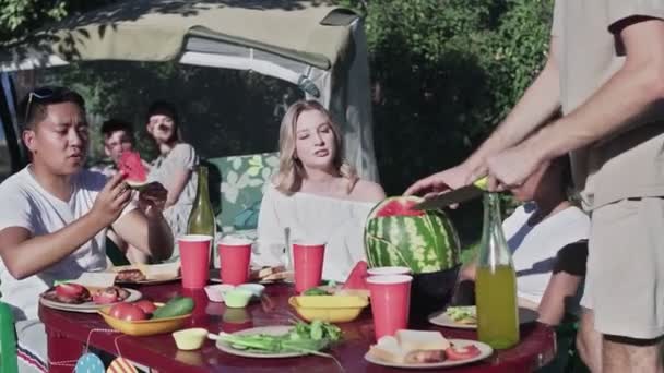 Multi-ethnische Gruppe von Männern und Frauen beim Picknick beim Essen von Wassermelonen reden und lachen — Stockvideo