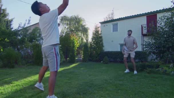 Двоє молодих чоловіків грають у бадмінтон на зеленому газоні на задньому дворі свого будинку — стокове відео