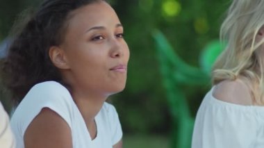 Arkadaşlarıyla şarkı söyleyen Afrikalı Amerikalı kadını yakından çek. Bir grup arkadaş parkta bir battaniyeye oturur.