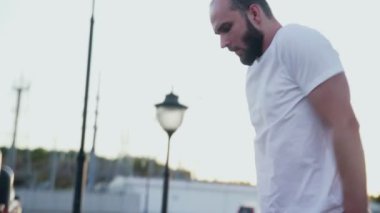 Beyaz tişörtlü genç adam şehir parkında antrenman yaparken yatay çubuğa yaklaşıyor..