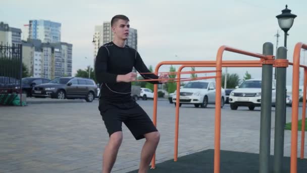 Joven musculoso haciendo ejercicios con banda elástica al aire libre. Entrenamiento — Vídeos de Stock