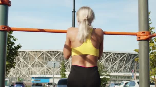 Vista posterior de la joven atleta se tira hacia arriba en la barra horizontal. Al aire libre. Entrenamiento — Vídeos de Stock